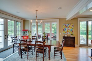 A dining room with a wooden table, chairs, and a chandelier. There is a large window with a view of the outdoors. - Stockbridge Retreat w/ Pool & Hot Tub! (Stockbridge)