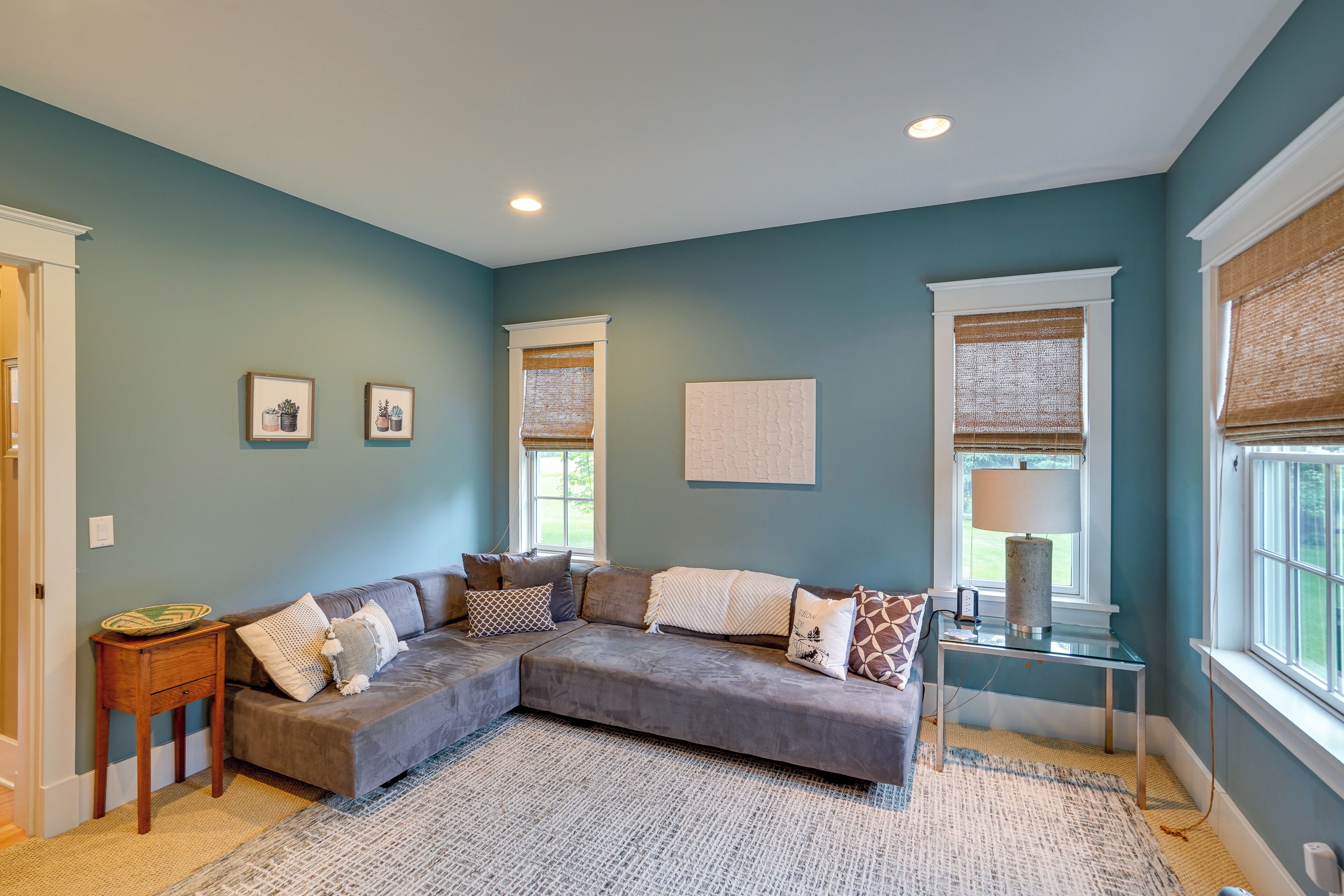 A living room with teal walls, a sectional sofa, a glass coffee table, and a small side table.