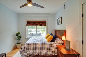 A bedroom with a bed, a ceiling fan, a window with blinds, a nightstand, a lamp, a potted plant, and a wall-mounted picture. - Stockbridge Retreat w/ Pool & Hot Tub! (Stockbridge)