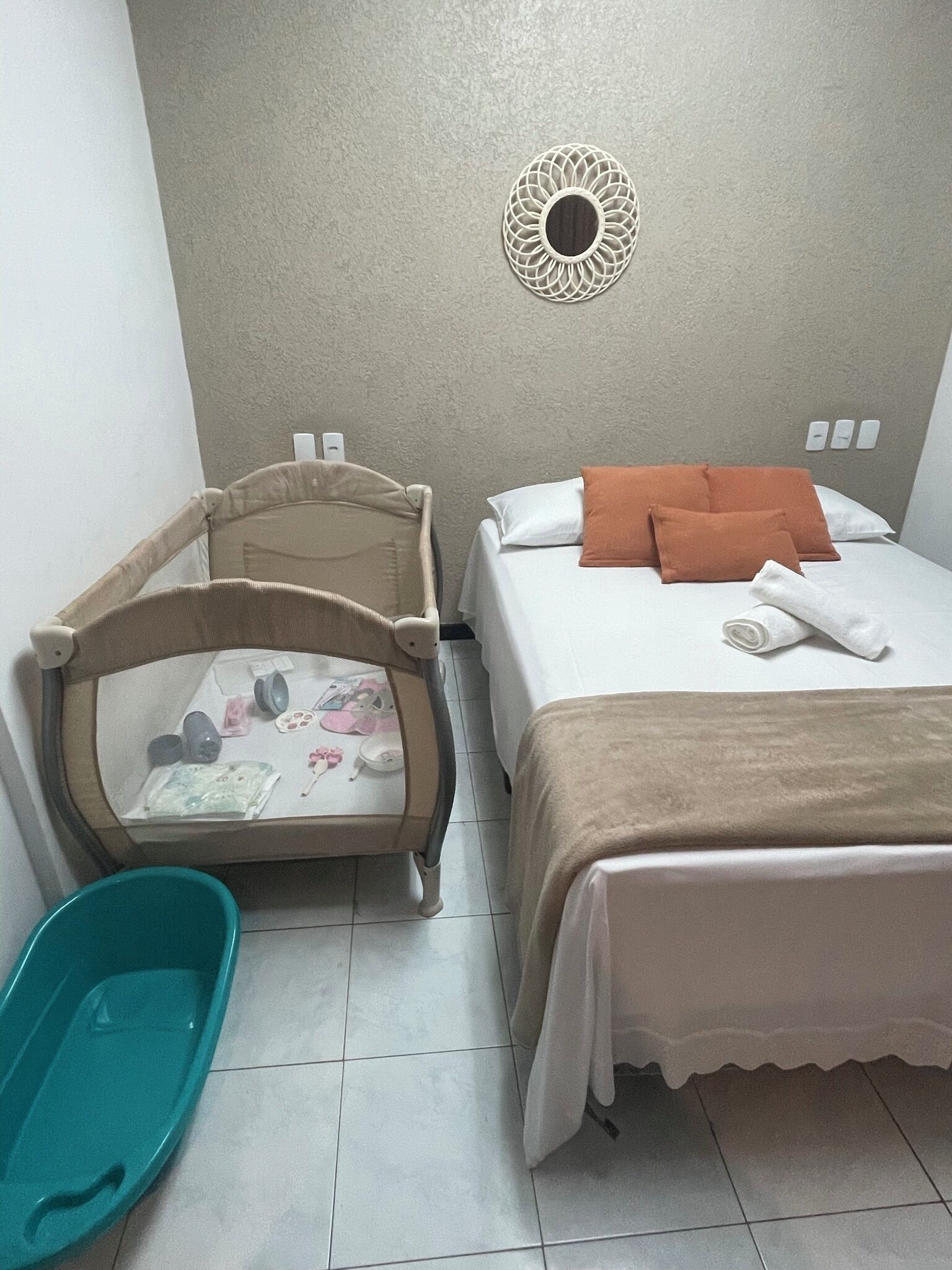 A bedroom with a bed, a crib, a wall-mounted decorative item, and a green plastic basin.
