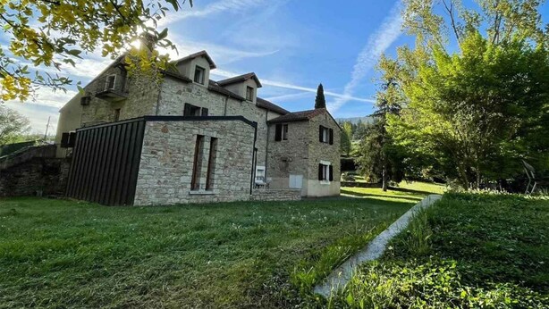 A stone house with a sloped roof, a small attached garage, and a well-maintained lawn. - Auberge de jeunesse HI Millau La Maladrerie (Millau)