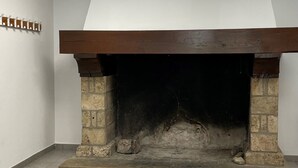 A room with a stone fireplace, tiled floor, white walls, and a ceiling light. - Auberge de jeunesse HI Millau La Maladrerie (Millau)