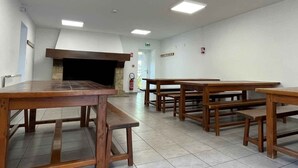 A spacious room with multiple wooden tables and benches, a fireplace, and tiled flooring. - Auberge de jeunesse HI Millau La Maladrerie (Millau)