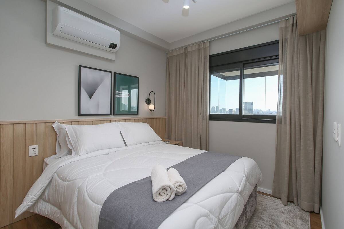 Ein Hotelzimmer mit Bett, Klimaanlage, Fenster mit Vorhängen und Blick auf die Stadt.