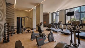 Une salle de sport moderne équipée de divers appareils d’exercice, dotée de grandes fenêtres et d’un téléviseur à écran plat.