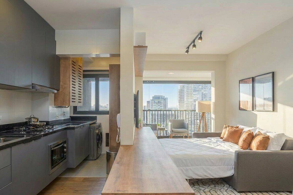 Eine moderne Küche mit einer zentralen Kochinsel, einem Essbereich mit langem Tisch, einer Couch und einem Balkon mit Blick auf die Stadt.