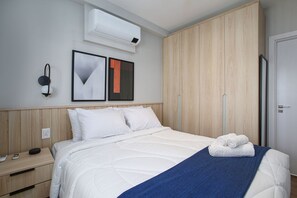 A hotel room with a bed, a nightstand, a wall-mounted air conditioner, and a wardrobe. - Expand Pinheiros (São Paulo)