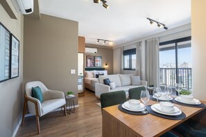 A modern living room with a dining area, a sofa, a chair, and a table set for dining. - Expand Pinheiros (São Paulo)