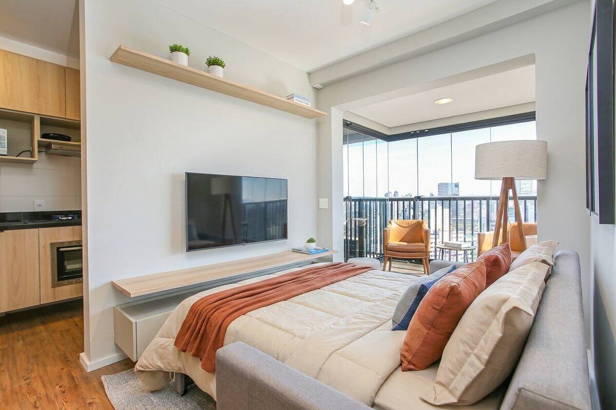 Ein modernes Hotelzimmer mit Bett, Fernseher, Balkon und Küchenzeile.