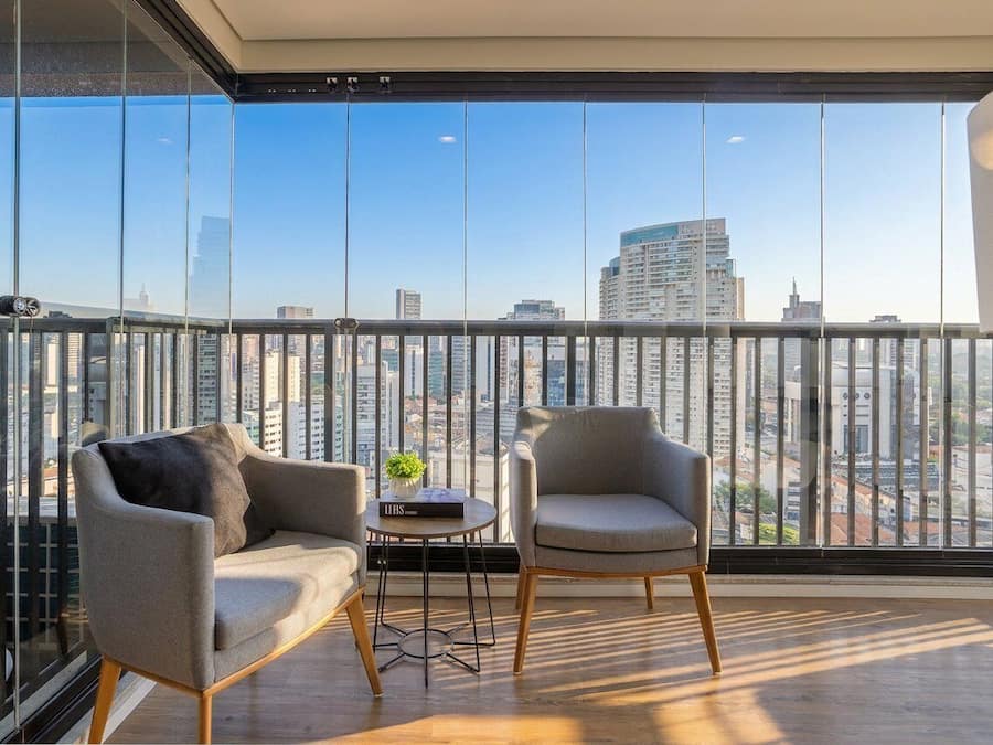 A balcony with two chairs, a small table, and a view of a cityscape through large windows.