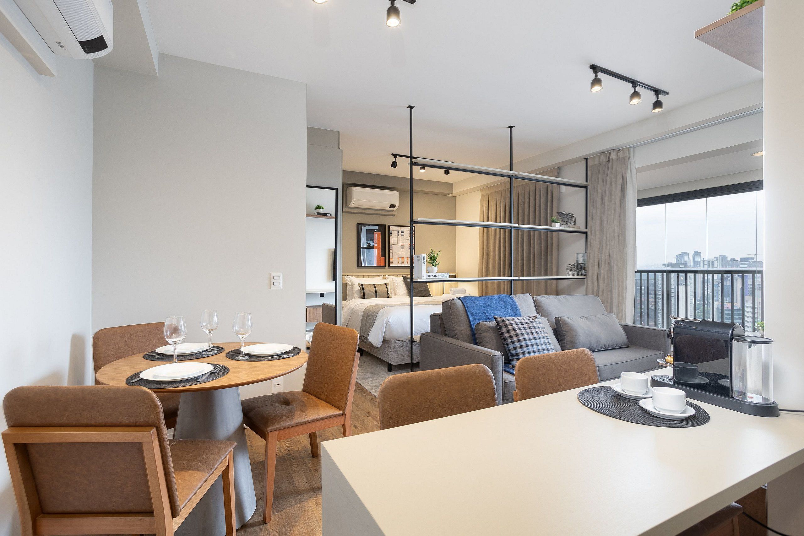 A modern hotel room with a dining area, a sofa, a bed, and a city view.