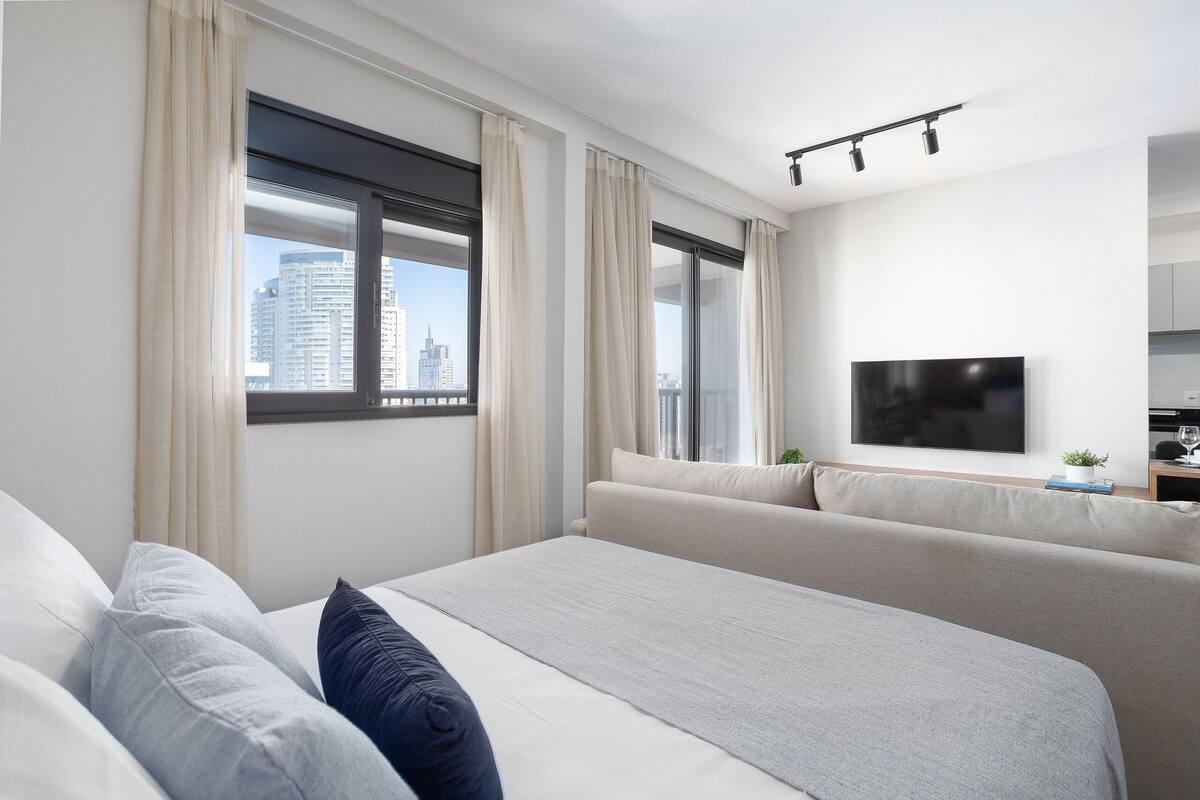 Ein modernes Hotelzimmer mit einem großen Bett, einer Couch, einem Fernseher und einem Fenster mit Vorhängen.
