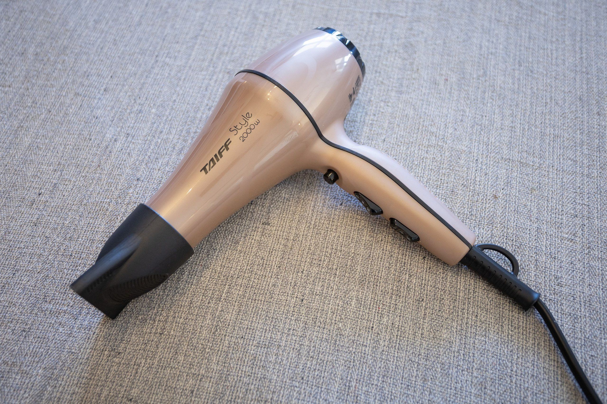 A hair dryer with a beige and black color scheme, lying on a textured surface.