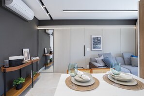 A modern living room with a sofa, a dining table set with plates and glasses, a coffee table, and a wall-mounted air conditioner. - Expand Pinheiros (São Paulo)