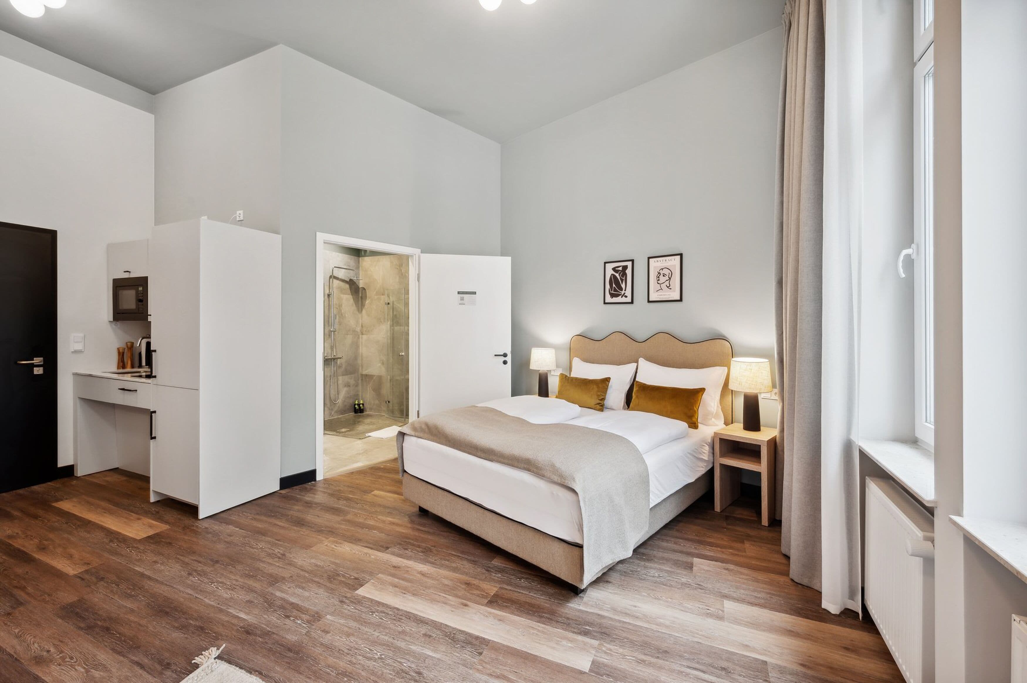 A modern hotel room with a large bed, bedside tables with lamps, a desk, and a shower area.
