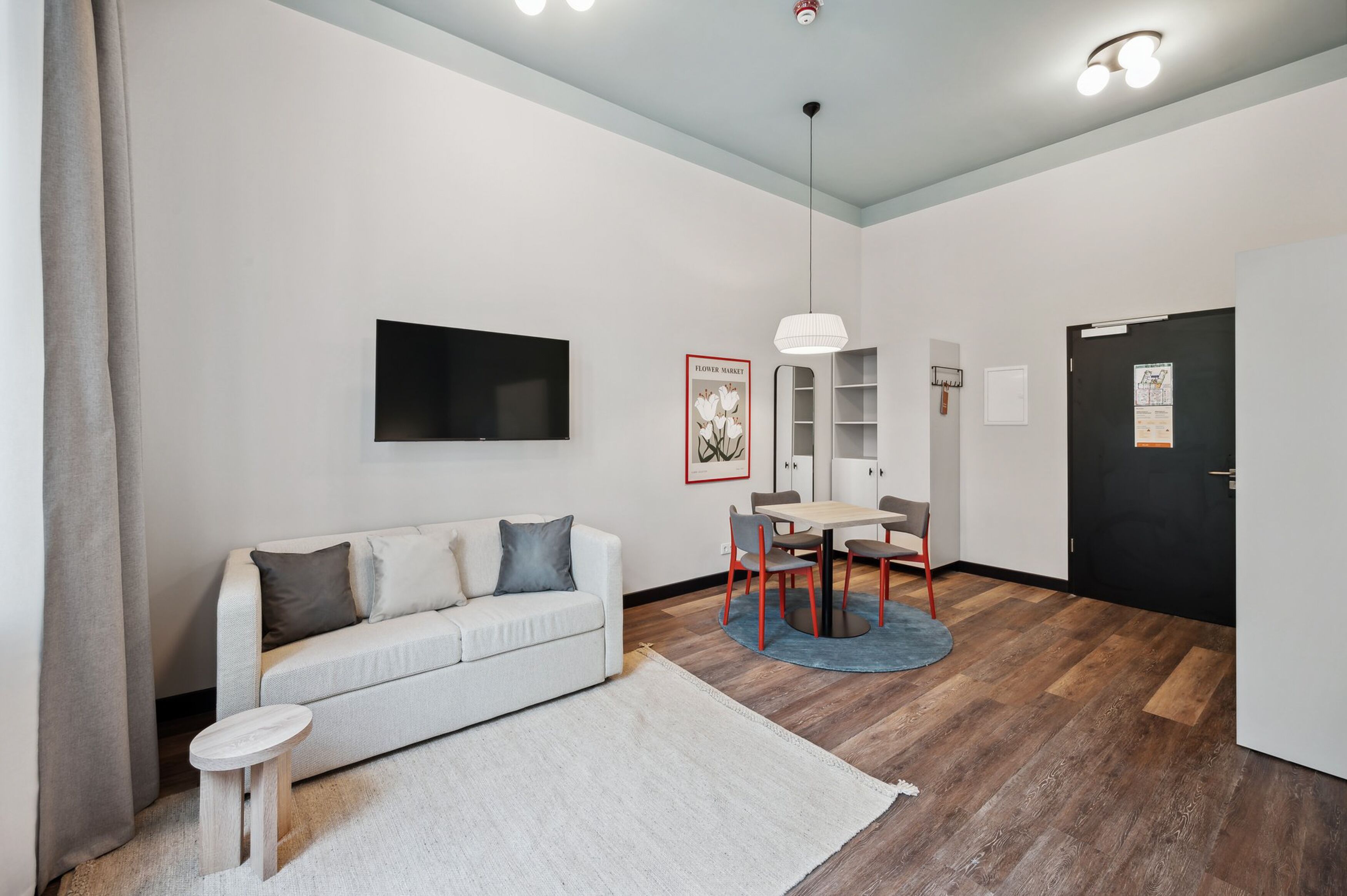 A modern living room with a sofa, a dining table, and a TV mounted on the wall.