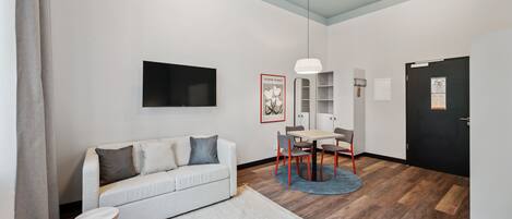 A modern living room with a sofa, a dining table, and a TV mounted on the wall.