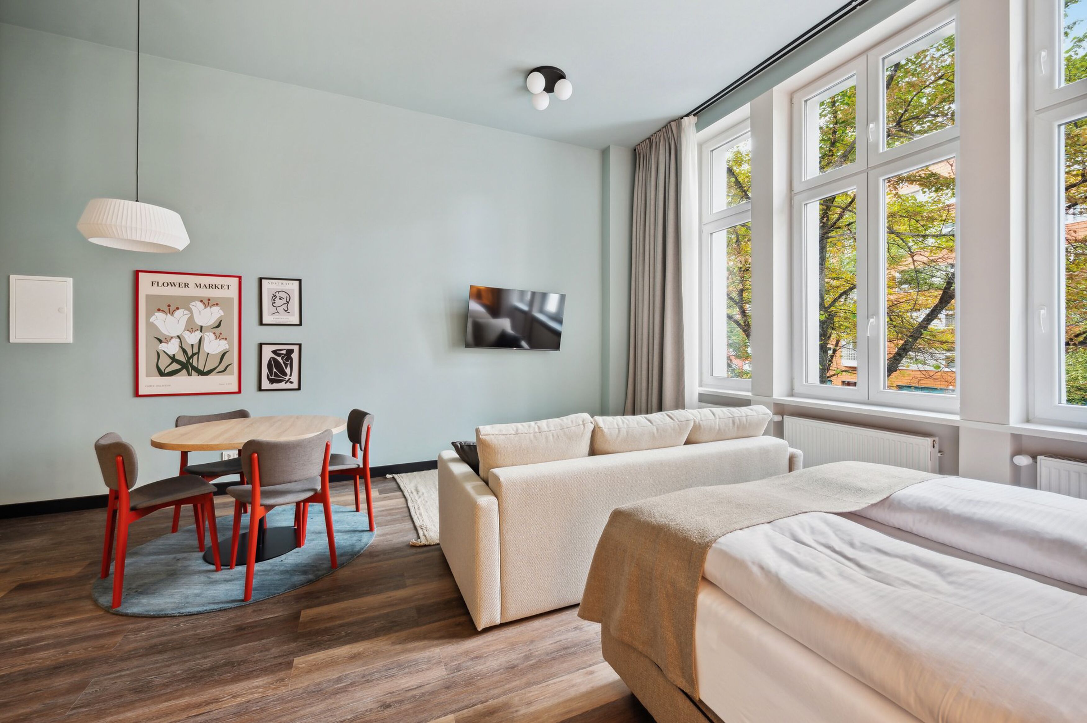 Una habitación de hotel moderna con comedor, sofá, cama y ventanas grandes con vista a árboles.