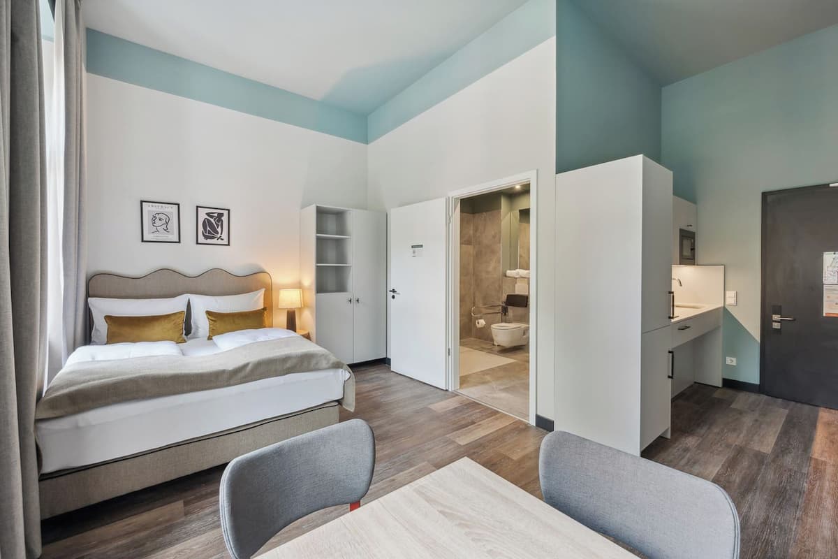 Habitación de hotel con cama, escritorio y baño visible a través de una puerta abierta.