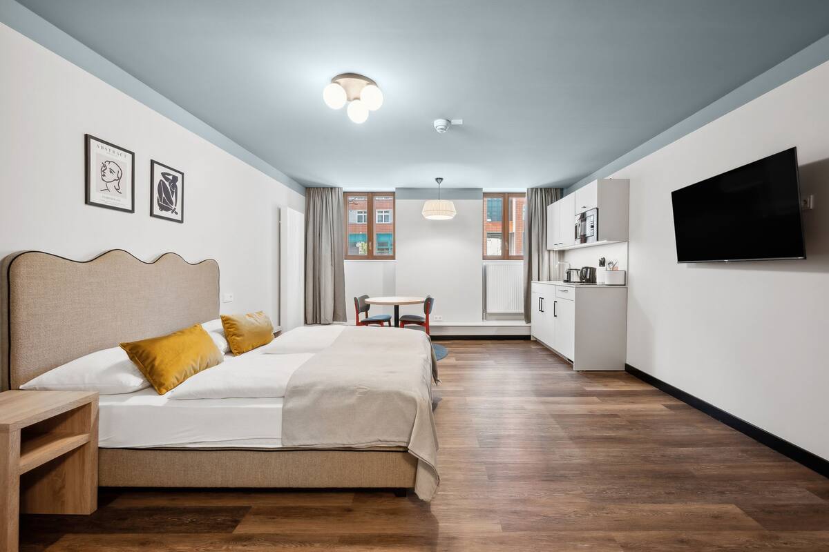 Una habitación de hotel con una cama, un escritorio, una silla, un televisor y una kitchenette.