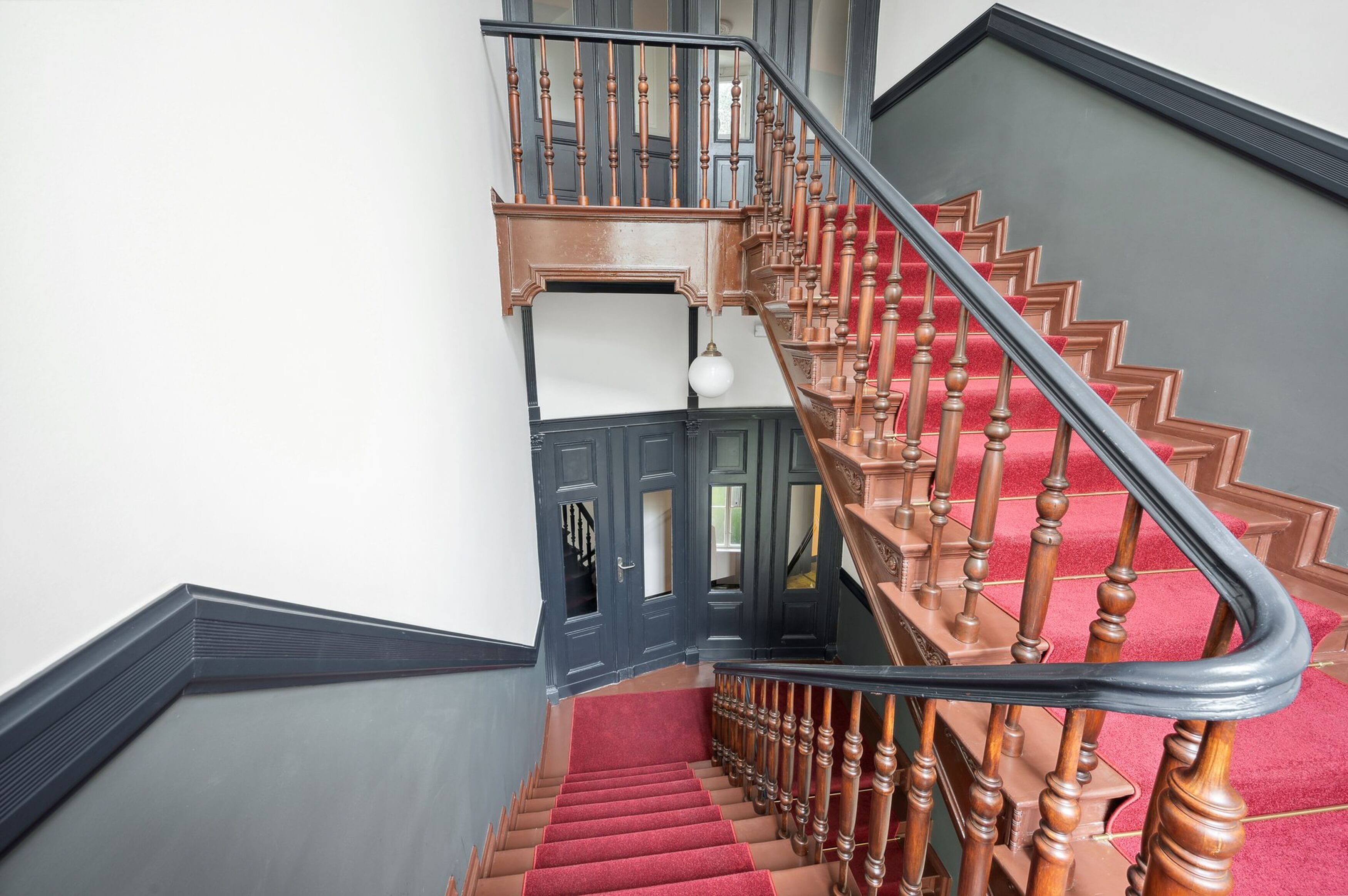 A grand staircase with a red carpet, wooden balusters, and a black handrail.