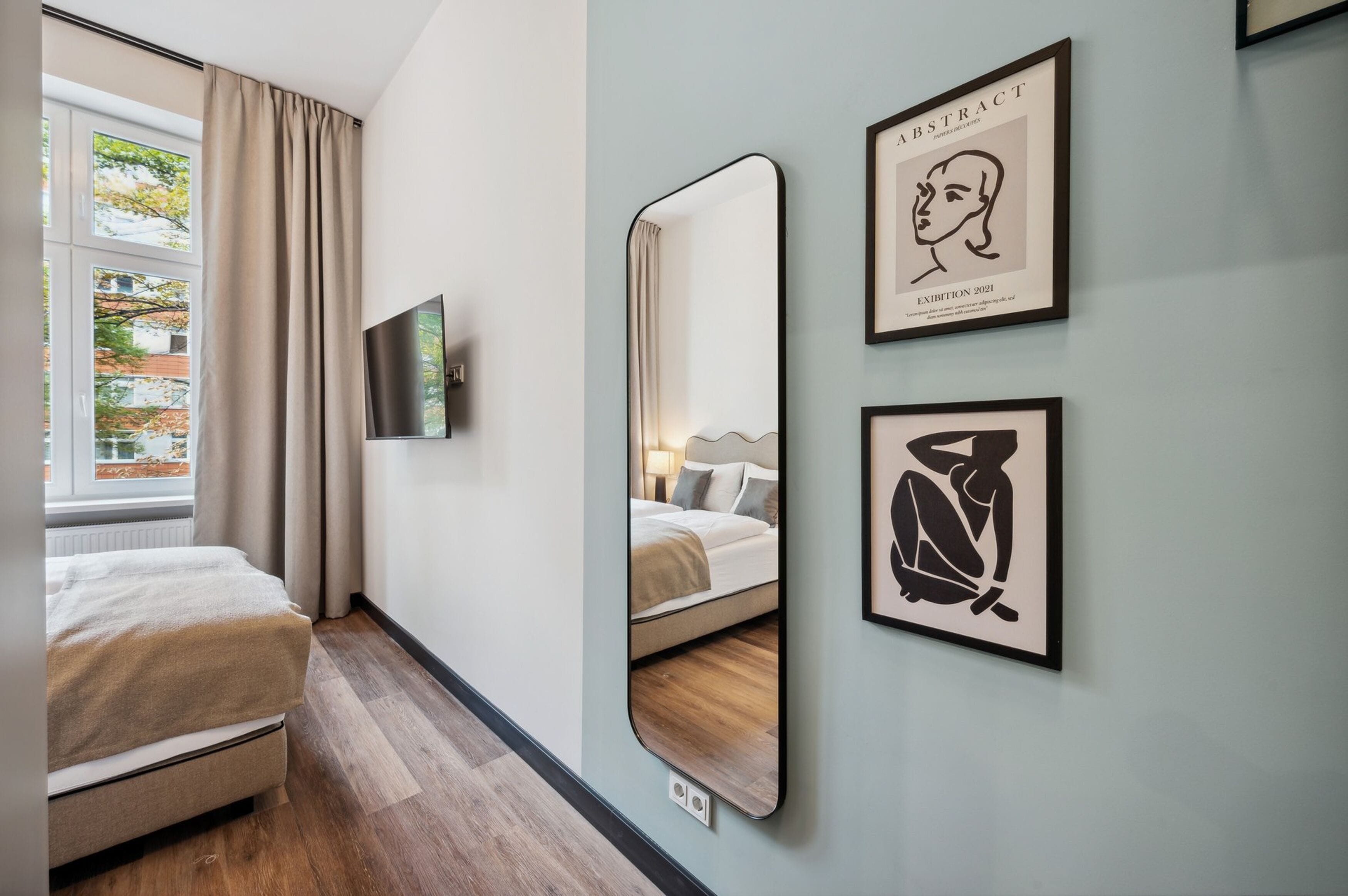 A hotel room with a bed, a large mirror, and two framed artworks on the wall.