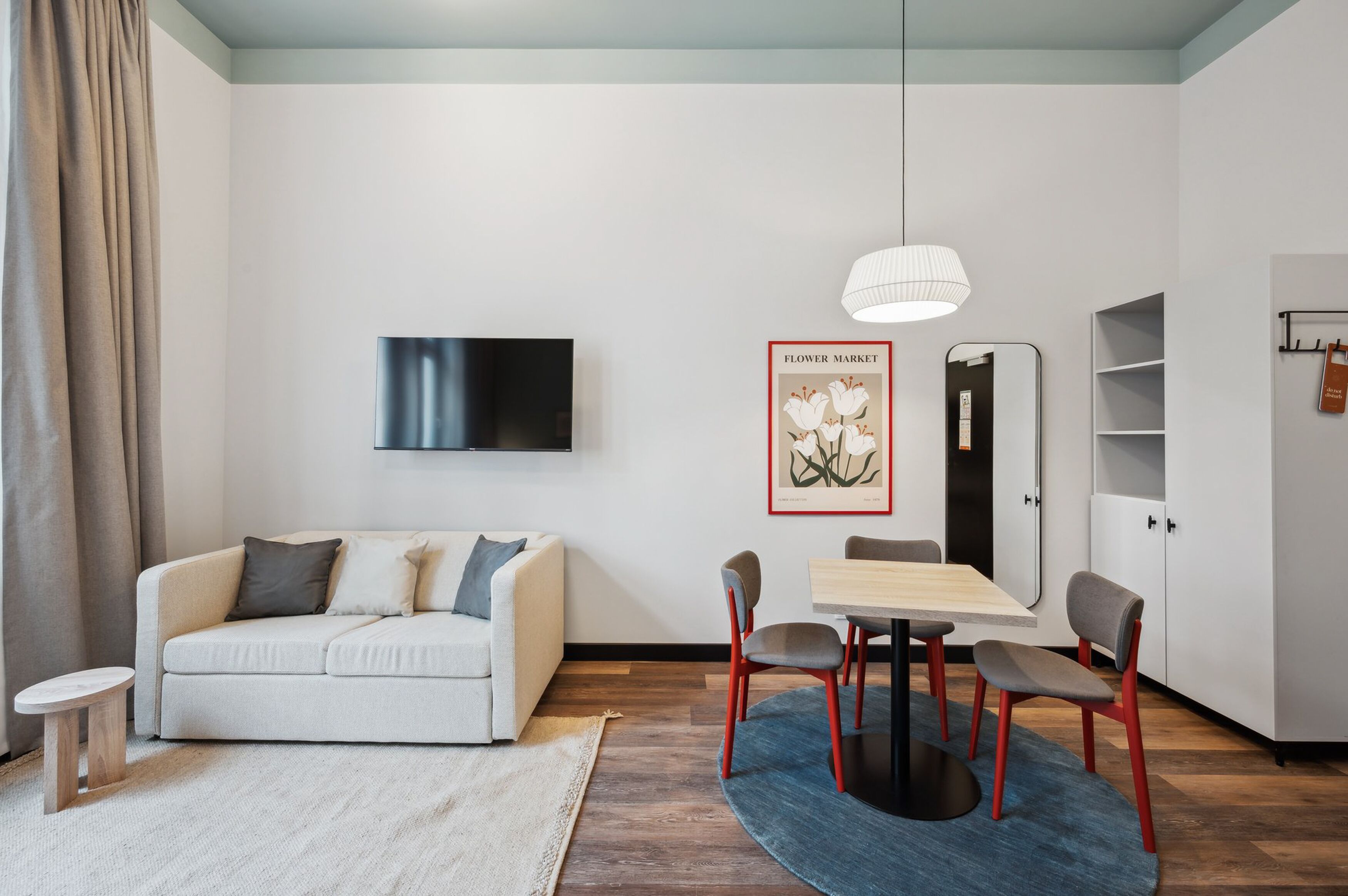 Ein modernes Wohnzimmer mit einer Couch, einem Esstisch mit Stühlen, einem an der Wand montierten Fernseher und einem Bilderrahmen mit Blumen.