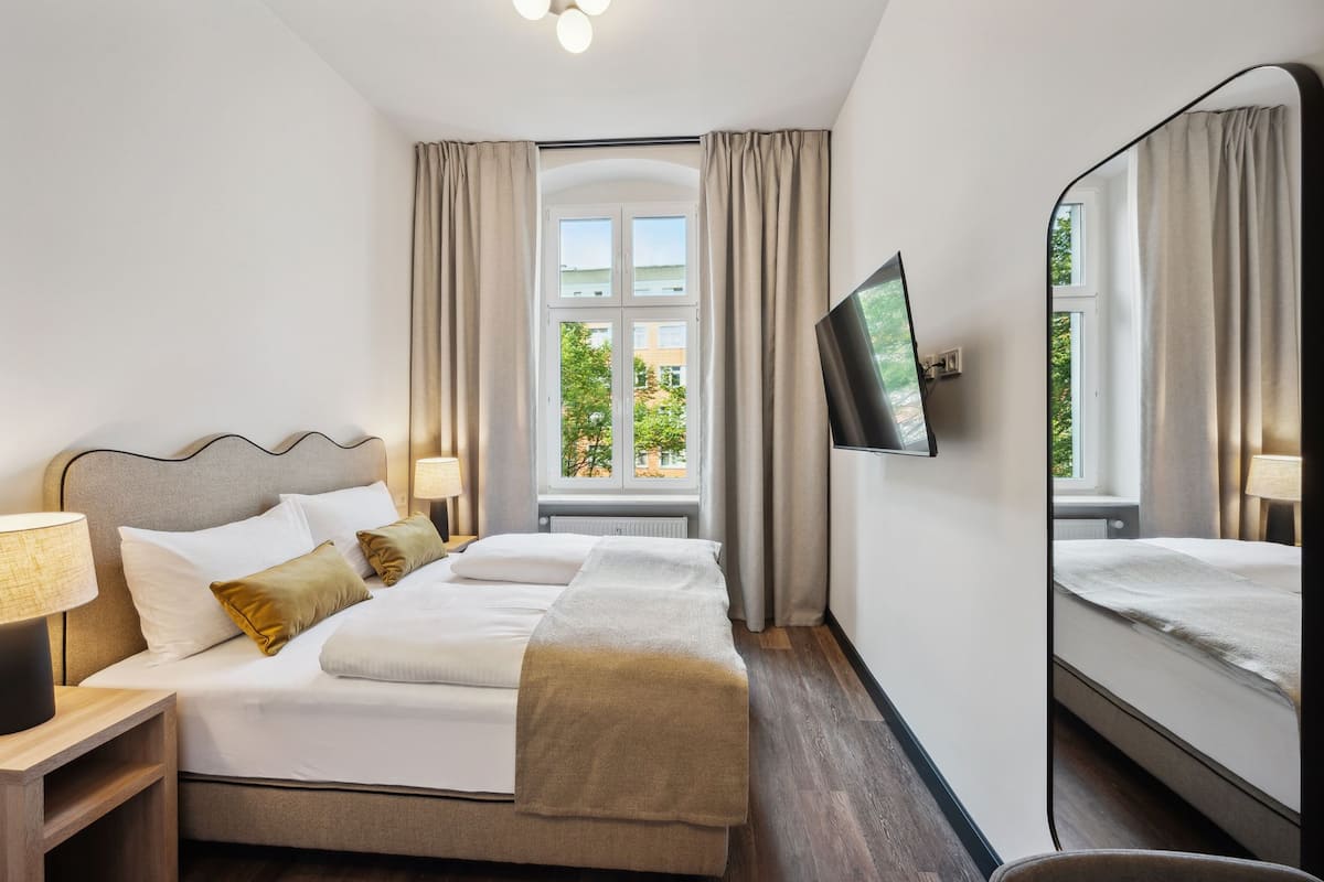 Habitación de hotel con una cama grande, un televisor montado en la pared y una ventana con cortinas.
