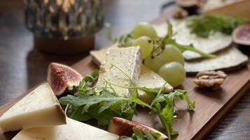 Ein Holzbruch mit Käse, Trauben und Salat, begleitet von einem Glaslaternen-Halter.