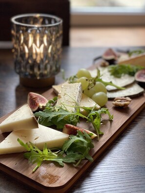 A wooden board with cheese, grapes, and greens, accompanied by a glass candle holder. - LE 120 (La Chataigneraie)