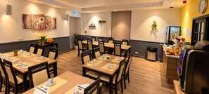 A hotel dining area with multiple tables, chairs, and a buffet counter. - LE 120 (La Chataigneraie)