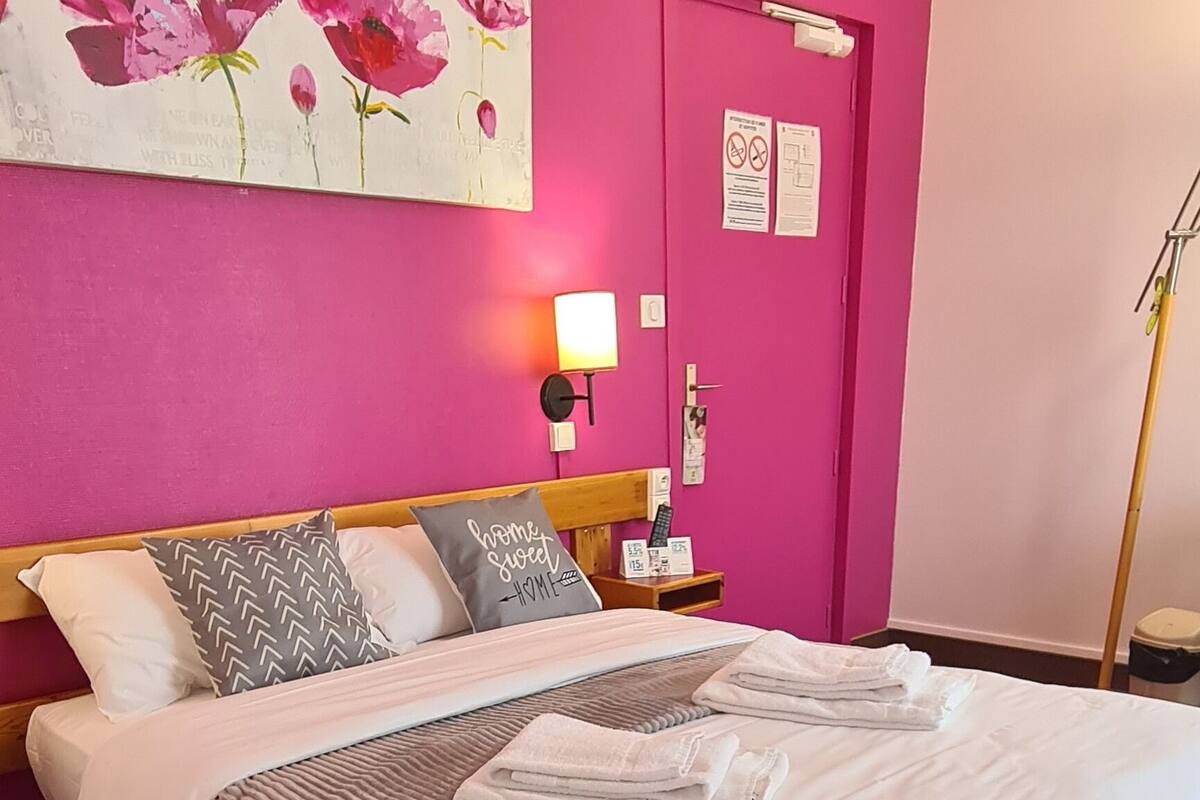 A bedroom with a large bed, pink walls, and a floral painting.
