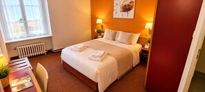 A hotel room with a bed, bedside tables, a radiator, a window, and a painting on the wall. - LE 120 (La Chataigneraie)