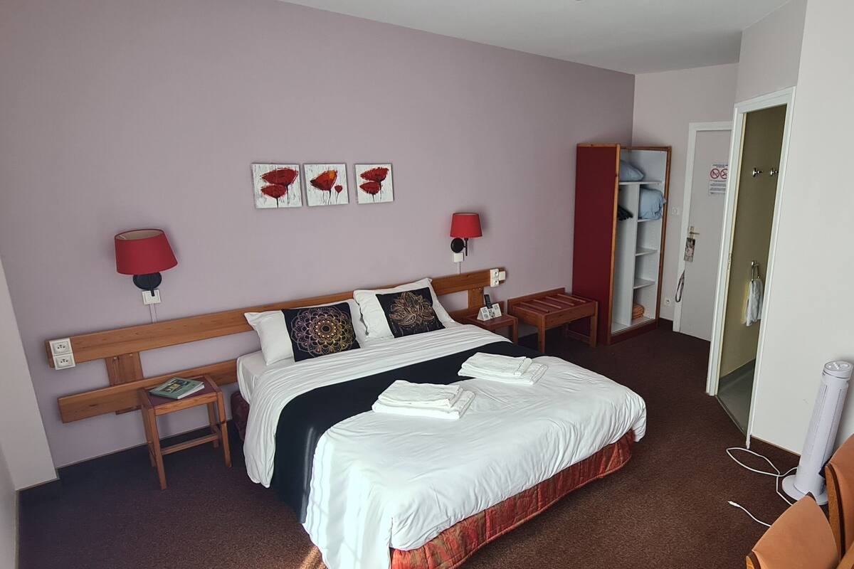A hotel room with a bed, bedside tables, a wardrobe, a desk with a chair, a lamp, and a wall-mounted TV.
