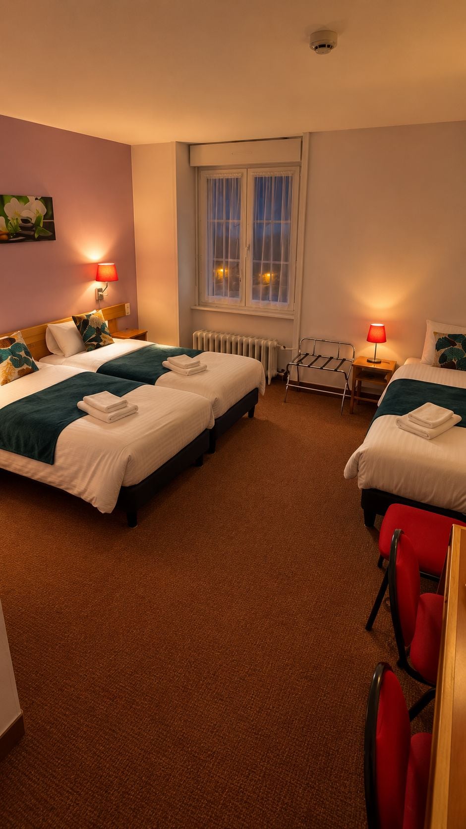 A hotel room with two beds, a radiator, a window with curtains, and a red chair.