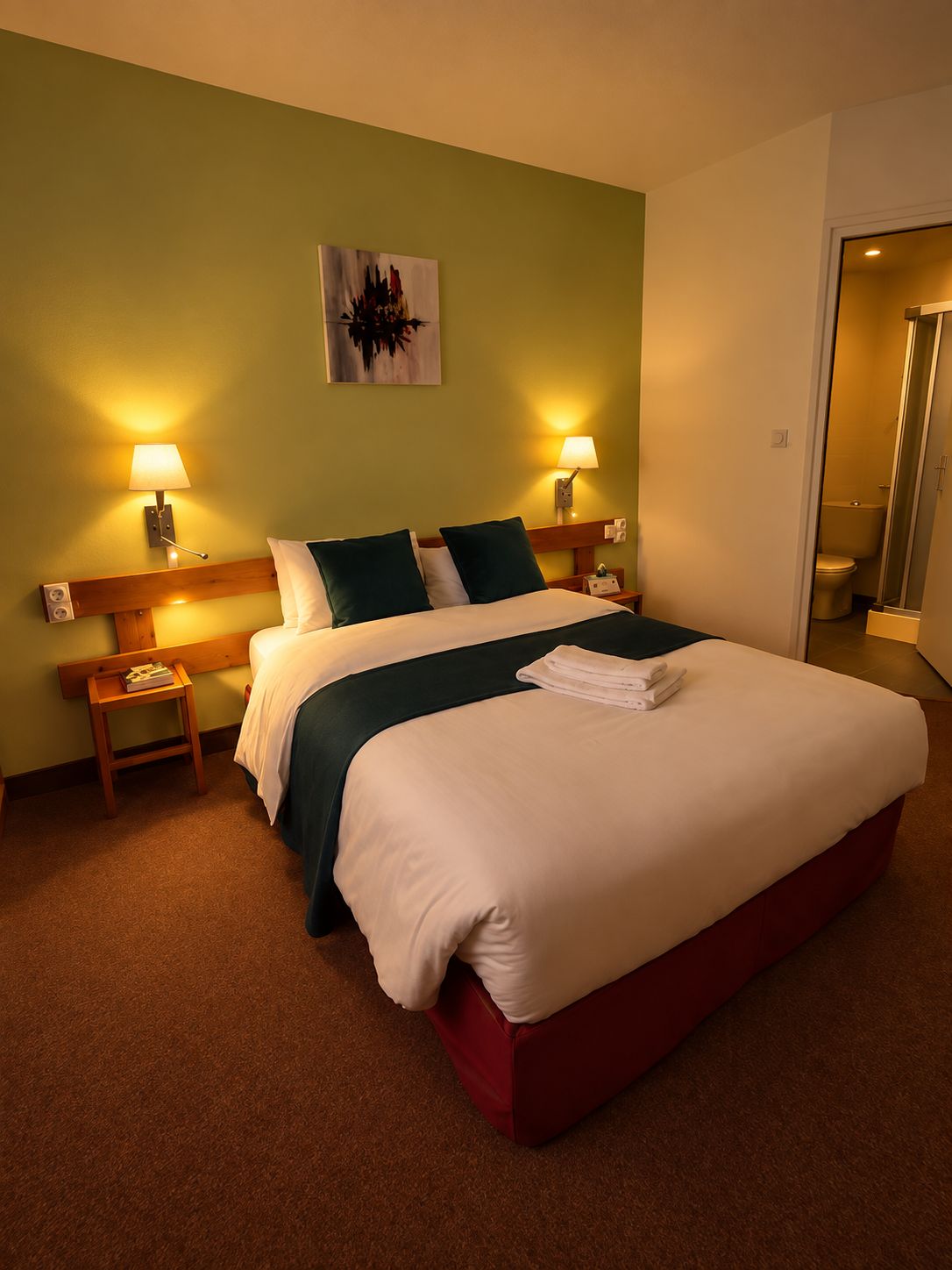Una habitación de hotel con una cama grande, dos mesitas de noche, un aparador, un cuadro en la pared y la puerta del baño.