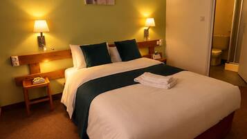 Una habitación de hotel con una cama grande, dos mesitas de noche, un aparador, un cuadro en la pared y la puerta del baño.