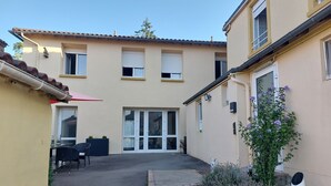 Ein Gebäude mit einem Ziegeldach, einer überdachten Terrasse mit Tisch und Stühlen sowie einem Gartenbereich mit Lavendelpflanzen.