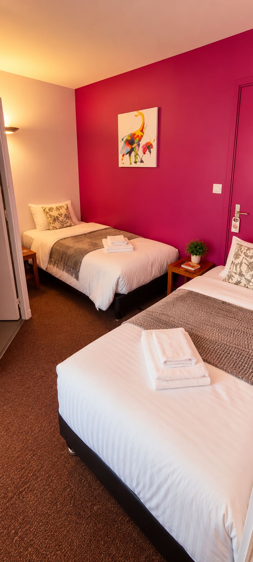 A hotel room with two beds, a red accent wall, and a painting of birds.