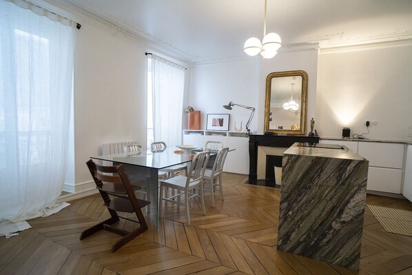 Uma área de refeições moderna com mesa de vidro, cadeiras de madeira e ilha de mármore.