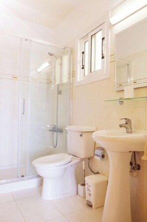 Een badkamer met een douche met glazen wand, toilet en een wastafel op een zuil.