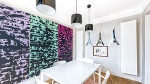 Zona de menjador moderna amb taula i cadires blanques, obra d'art abstracta de colors a la paret i llums penjants.