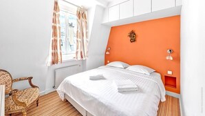 Una habitació d'hotel amb un llit gran, una cadira, una finestra amb cortines i una paret taronja decorativa.