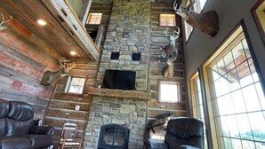 A rustic interior with a stone fireplace, leather seating, and mounted deer heads. - Stunning Lodge Experience in Buffalo County WI/Picturesque Views-Pet Friendly! (Mondovi)