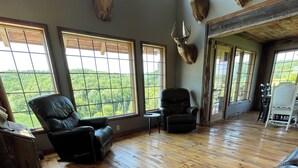A spacious living room with wooden flooring, two leather sofas, a wooden coffee table, and large windows offering a view of the outdoors. - Stunning Lodge Experience in Buffalo County WI/Picturesque Views-Pet Friendly! (Mondovi)