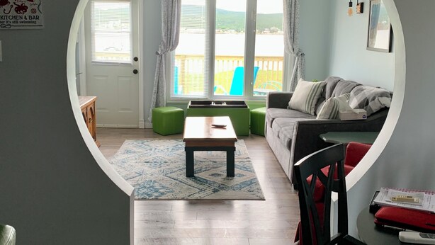 Een woonkamer met een rond raam, een bank, een salontafel, en een eetgedeelte met een stoel en tafel.