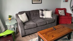 Een woonkamer met een grijze bank, een rode fauteuil, een houten salontafel en een bijzettafeltje met een plant.