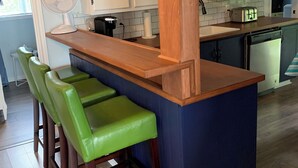 Een keuken met een houten kookeiland, groene barstoelen, witte kasten en een ventilator.