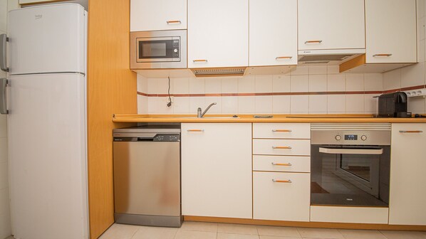 Cozinha equipada com geladeira, micro-ondas, lava-louças, forno e bancada de madeira.