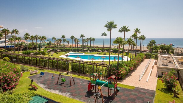 Um resort com piscina, palmeiras e vista para a praia.
